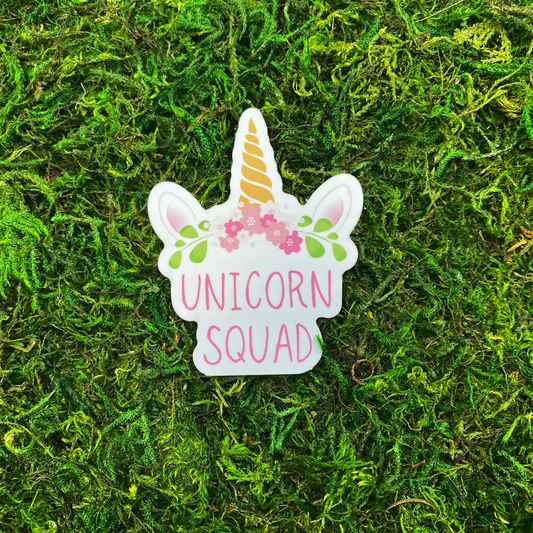 Die-cut vinyl sticker featuring a white unicorn face with a gold swirled horn, pink floral crown, and the words "Unicorn Squad" in pink lettering, photographed on a bed of green moss.