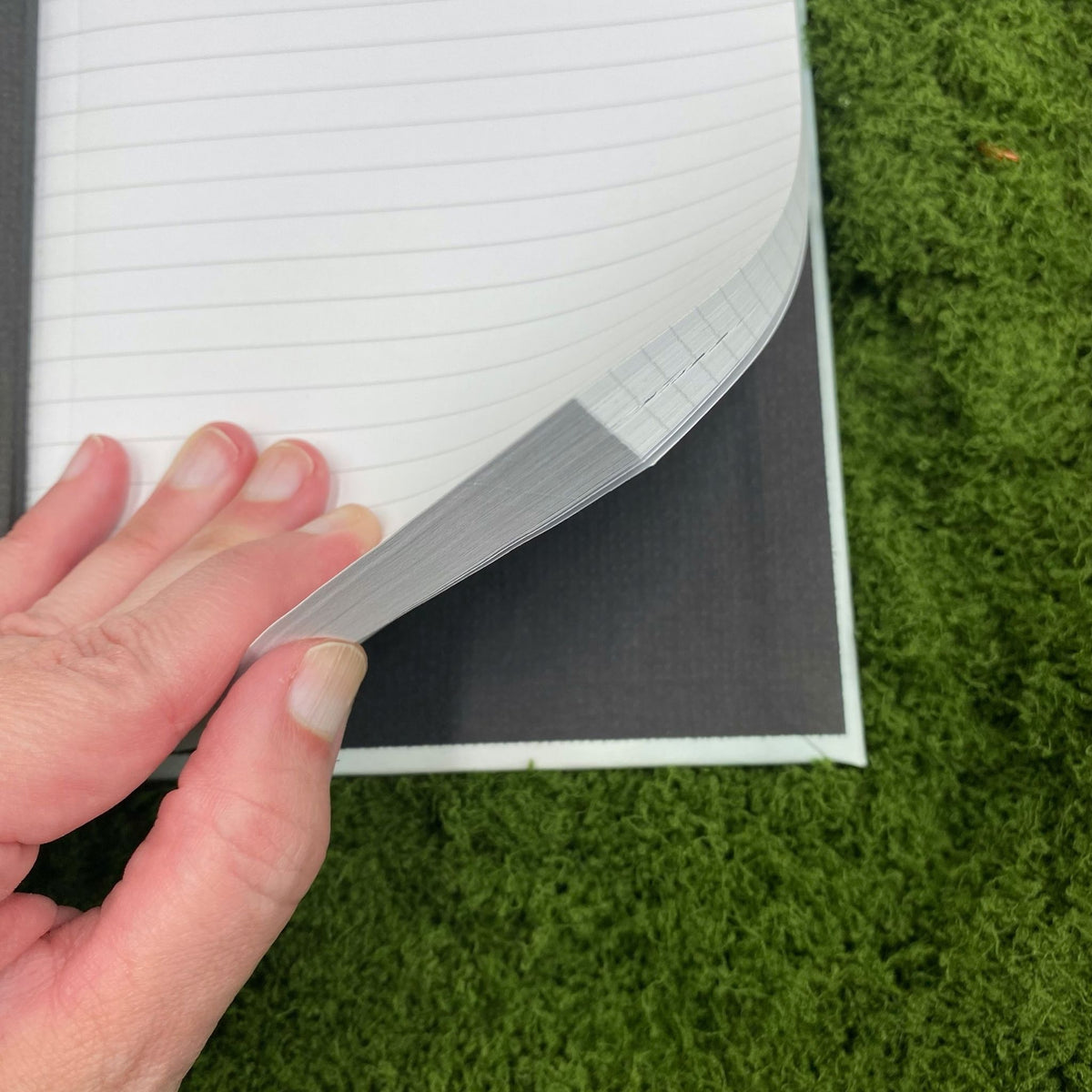 Close-up of a hand lifting a lined page in the journal, showing the black interior lining of the hardcover binding.
