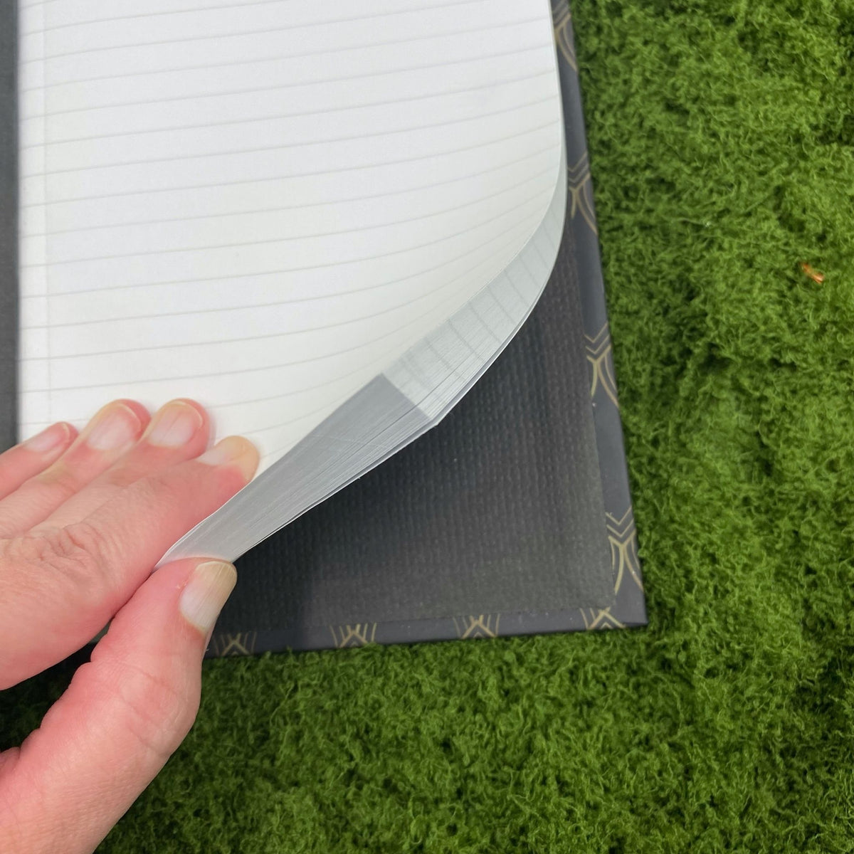 Close-up of a hand lifting a lined page in the journal, showing the black interior lining of the hardcover binding.