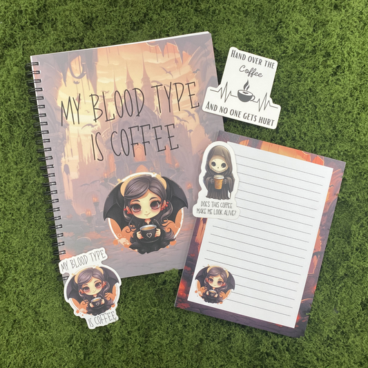 A gothic desk gift set including a my blood type is coffee spiral notebook, a matching 5x7 lined notepad, and three die-cut stickers featuring a vampire girl, a grim reaper with coffee, and a hand over the coffee heartbeat monitor, arranged on a green moss surface