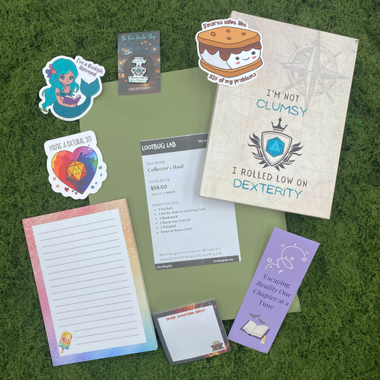 A Lootbug Lab studio bundle mystery bag with a reveal card surrounded by sample items including stickers, a bookmark, a pocket notebook, sticky note pads, and a greeting card on a green moss surface