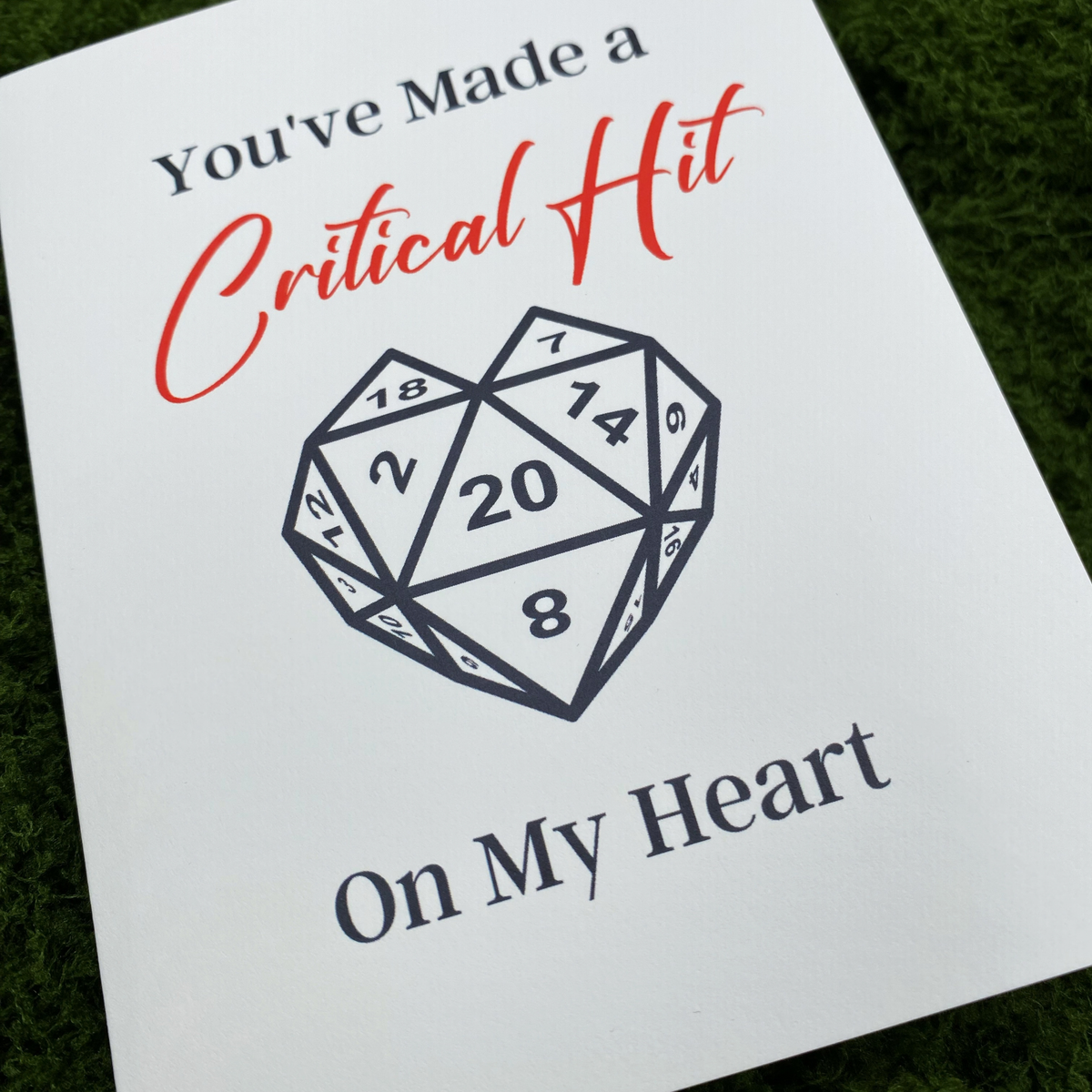 Close-up of the card's cover showing "You've Made a Critical Hit" in red script and "On My Heart" below a heart-shaped twenty-sided die with visible numbers including a 20 at center.
