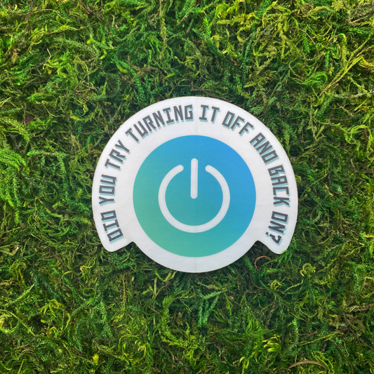A round sticker with a teal power button icon and the text "Did you try turning it off and back on?" resting on artificial moss.
