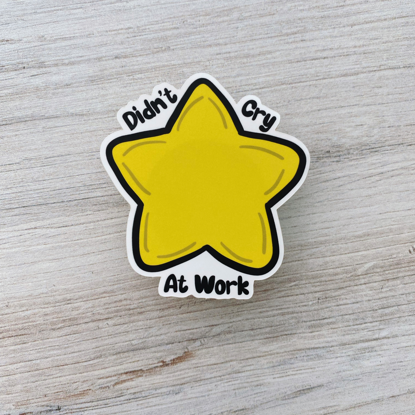 Die-cut vinyl sticker showing a yellow star, with the text "Didn't cry at work today," on a light wood background