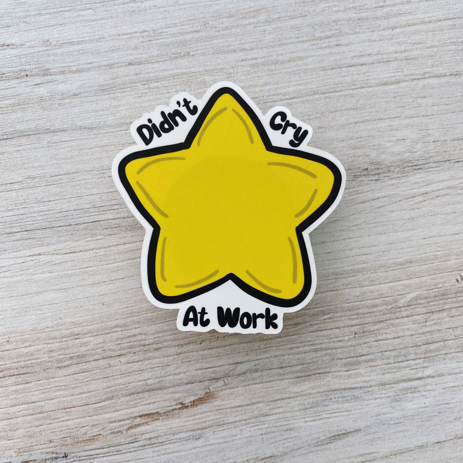 Die-cut vinyl sticker showing a yellow star, with the text "Didn't cry at work today," on a light wood background