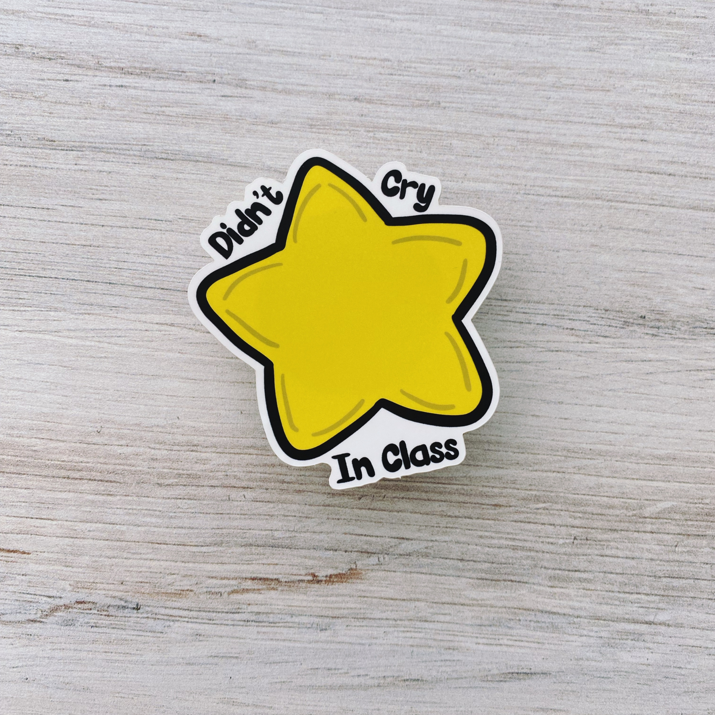 Die-cut vinyl sticker showing a yellow star, with the text "Didn't cry in class today," on a light wood background