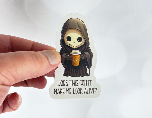 A hand holds a sticker illustration of a small hooded grim reaper holding a coffee cup, reading "Does this coffee make me look alive?" against a white background.