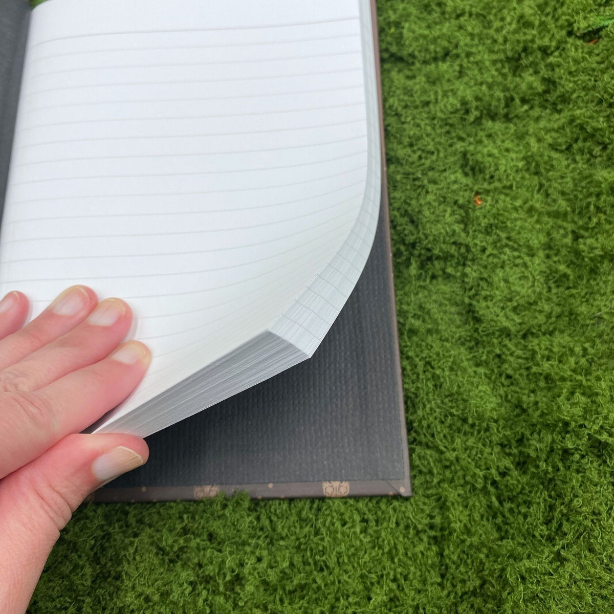 Close-up of a hand lifting a lined page in the journal, showing the plain paper lining on the inside cover.
