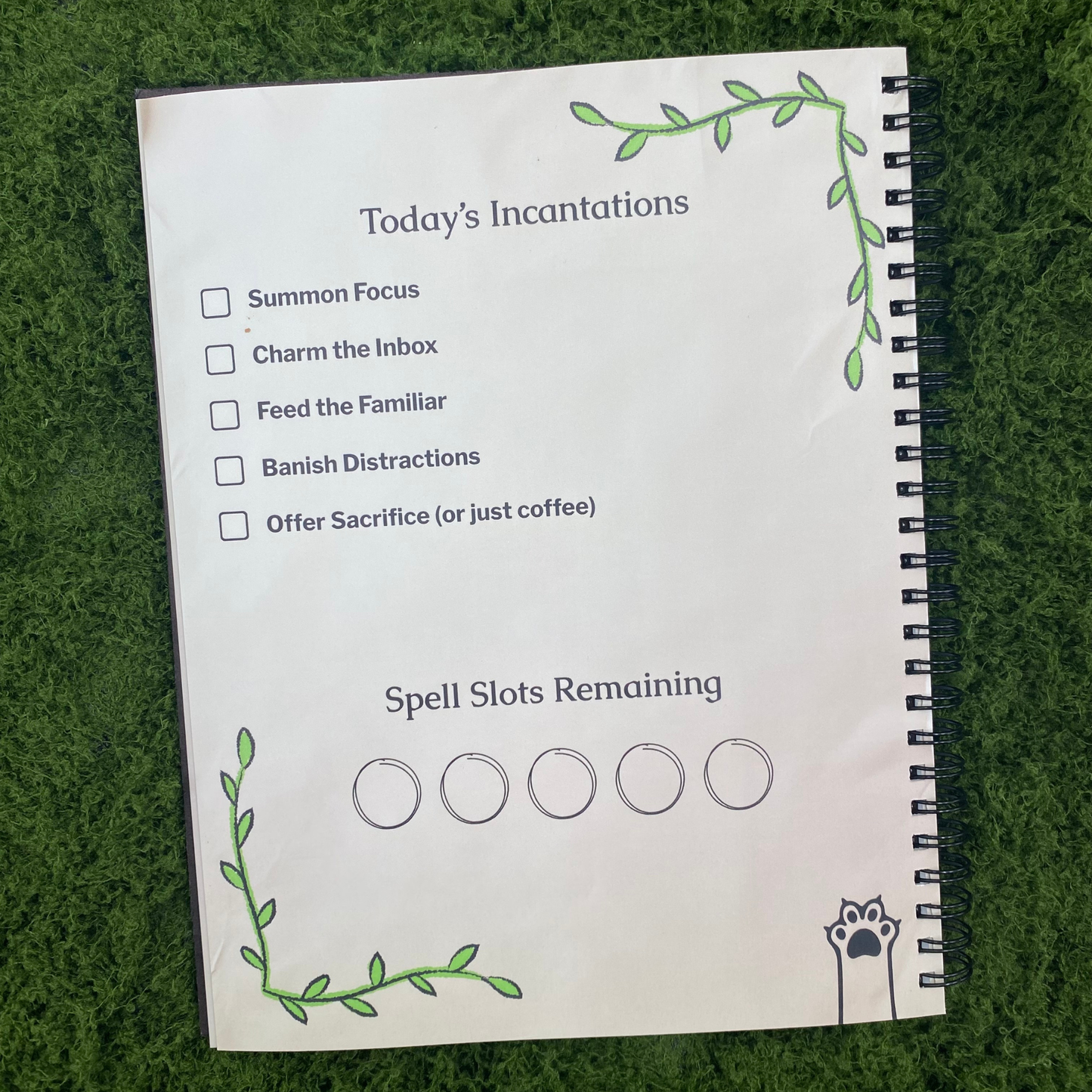 Inside front cover reading "Today's Incantations" with a checklist including "Summon Focus," "Charm the Inbox," and "Feed the Familiar," plus a "Spell Slots Remaining" tracker with five circles, framed by a green vine border.