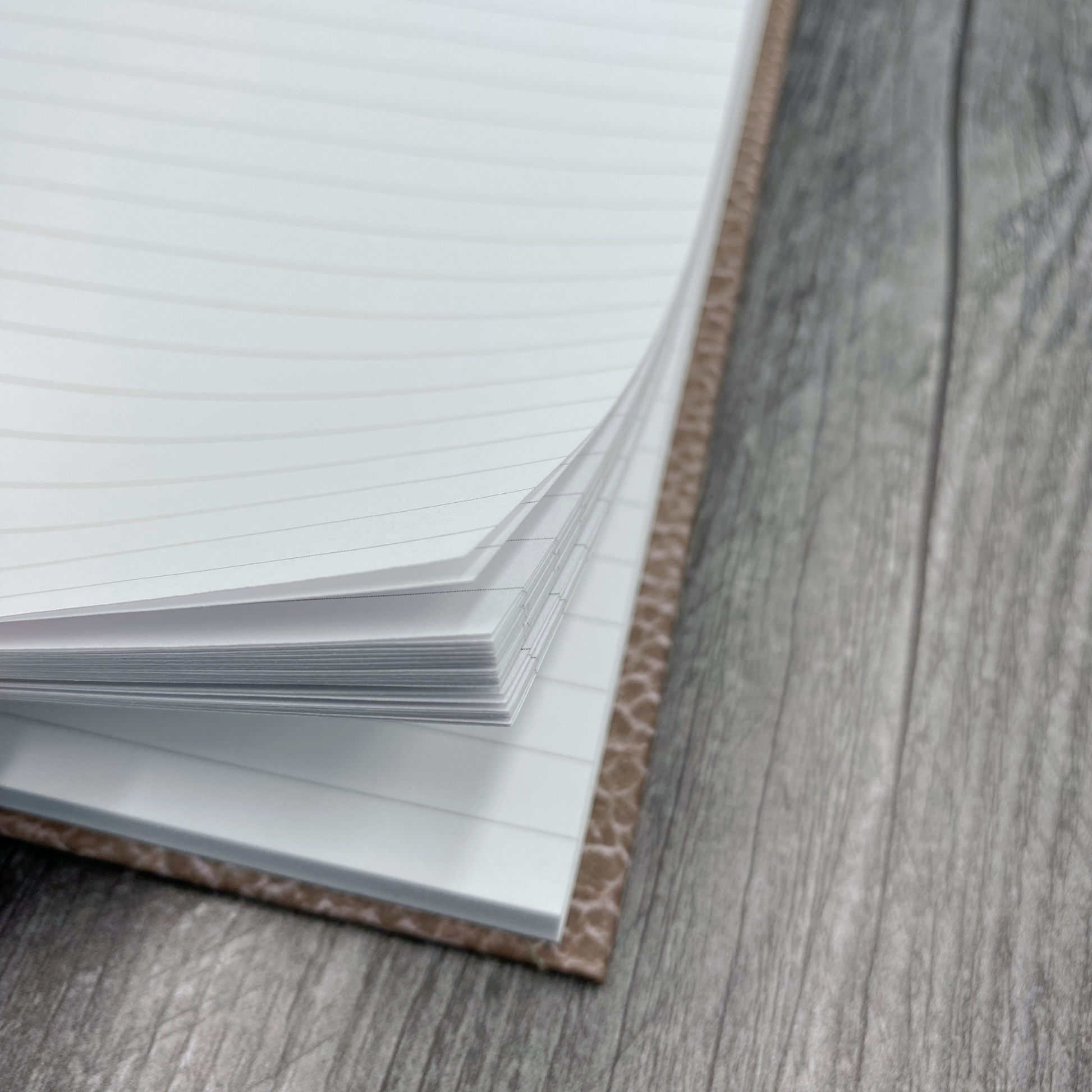 Close-up of lined pages inside a journal with a brown textured cover, on a wood surface.