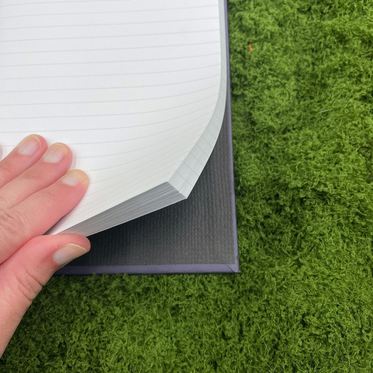 Close-up of a hand lifting a lined, perforated page in the navy journal, showing the black interior of the hardcover binding.