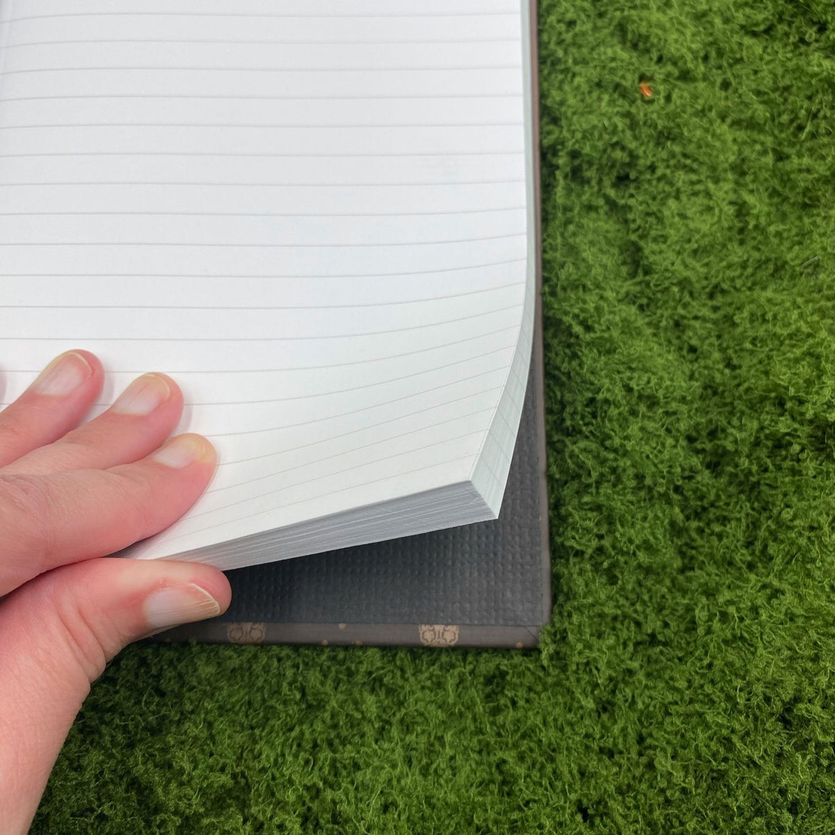 Close-up of a hand lifting a lined page in the journal, showing the plain paper lining on the inside cover.