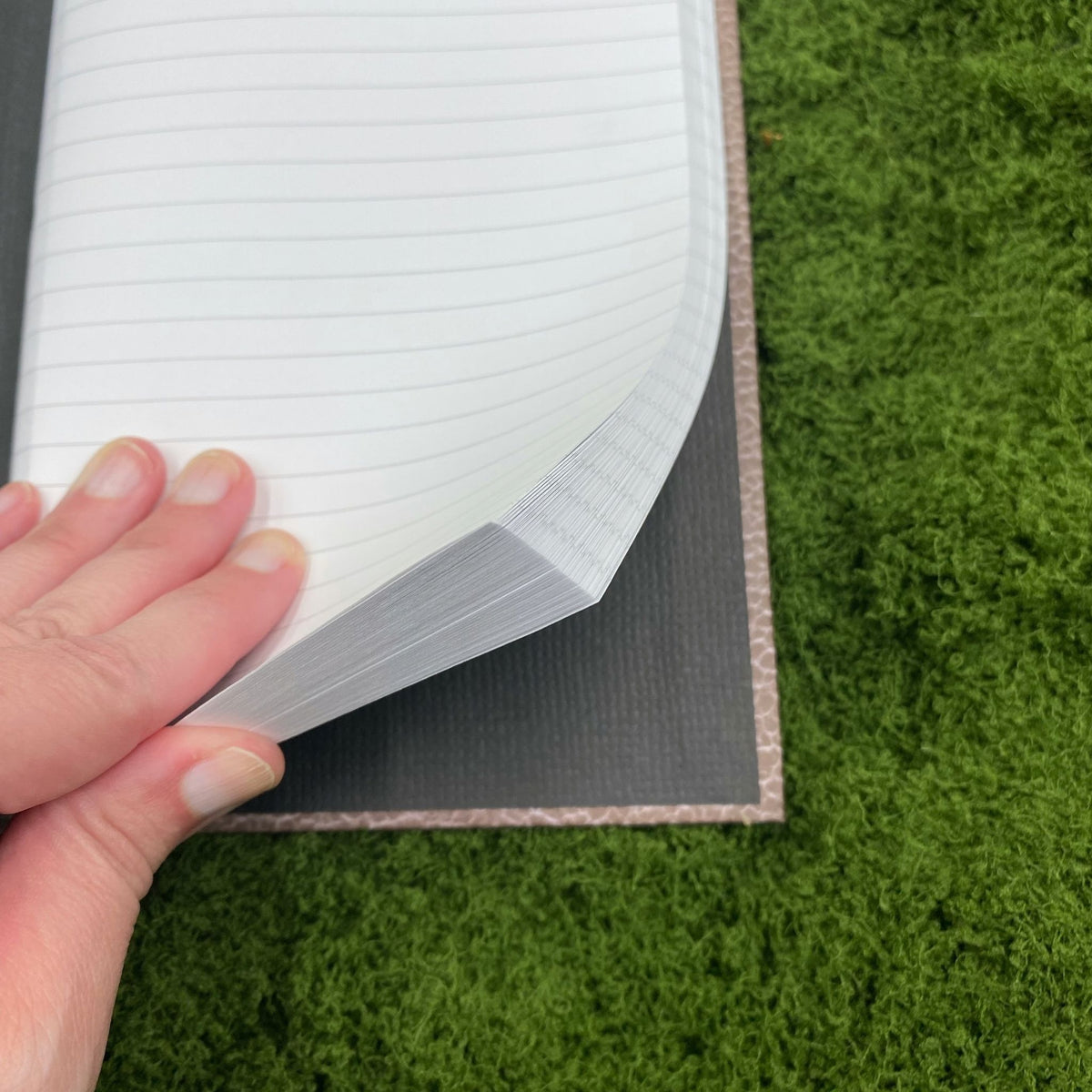 Close-up of a hand lifting a lined page in the journal, showing the black cardboard interior of the hardcover binding.