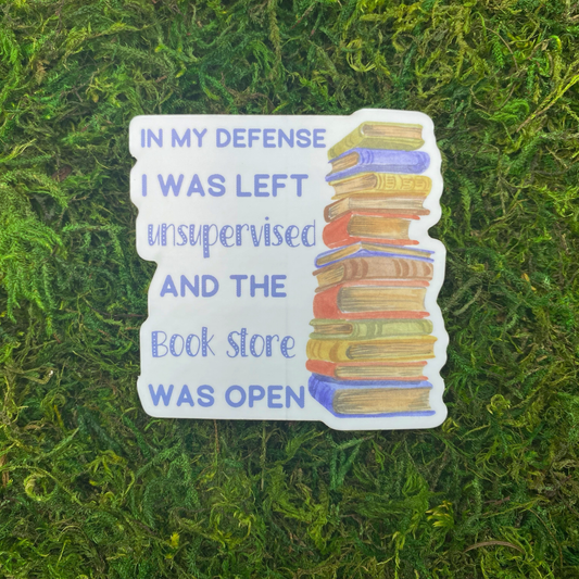 A sticker reading "In my defense I was left unsupervised and the book store was open" beside an illustration of a tall stack of books, resting on artificial moss.