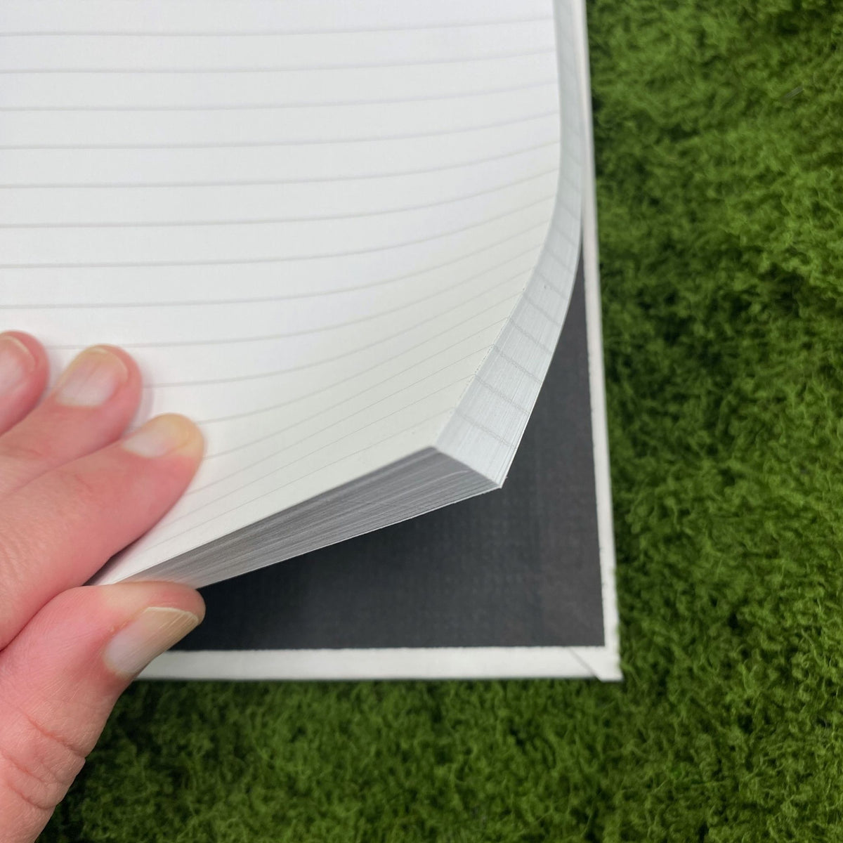 Close-up of a hand fanning through the lined pages of the journal, showing the black interior of the hardcover binding.