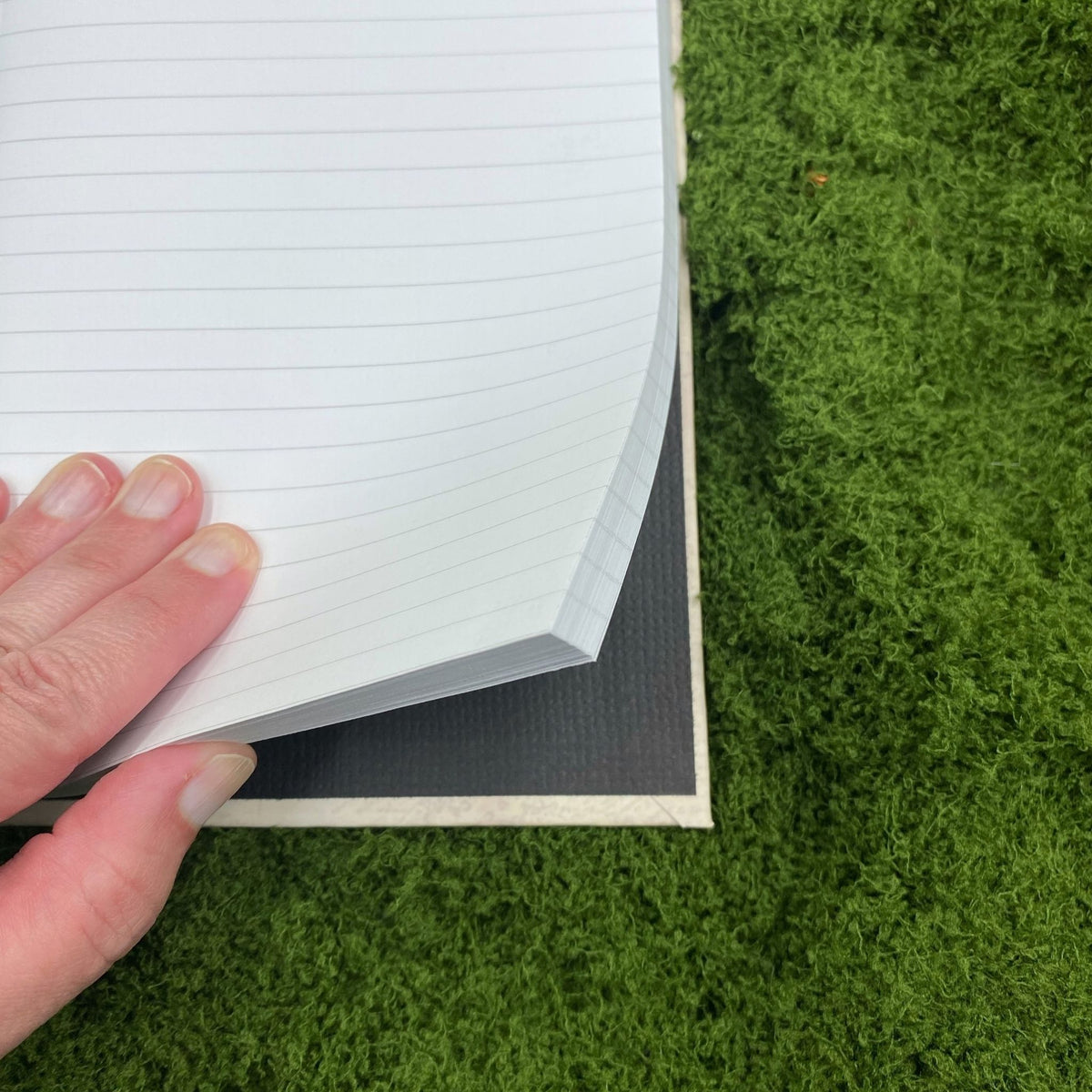 Close-up of a hand lifting a lined, perforated page in the journal, showing the black interior of the hardcover binding.