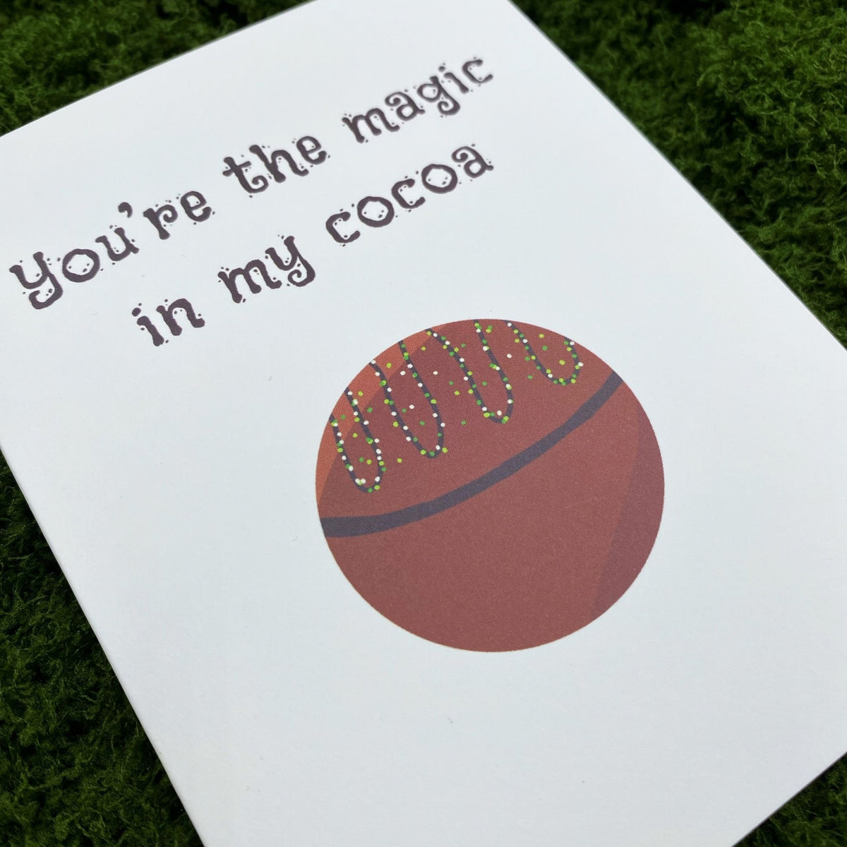 Close-up of the card's cover showing "You're the magic in my cocoa" above a round hot cocoa bomb drizzled with dotted sprinkle icing.