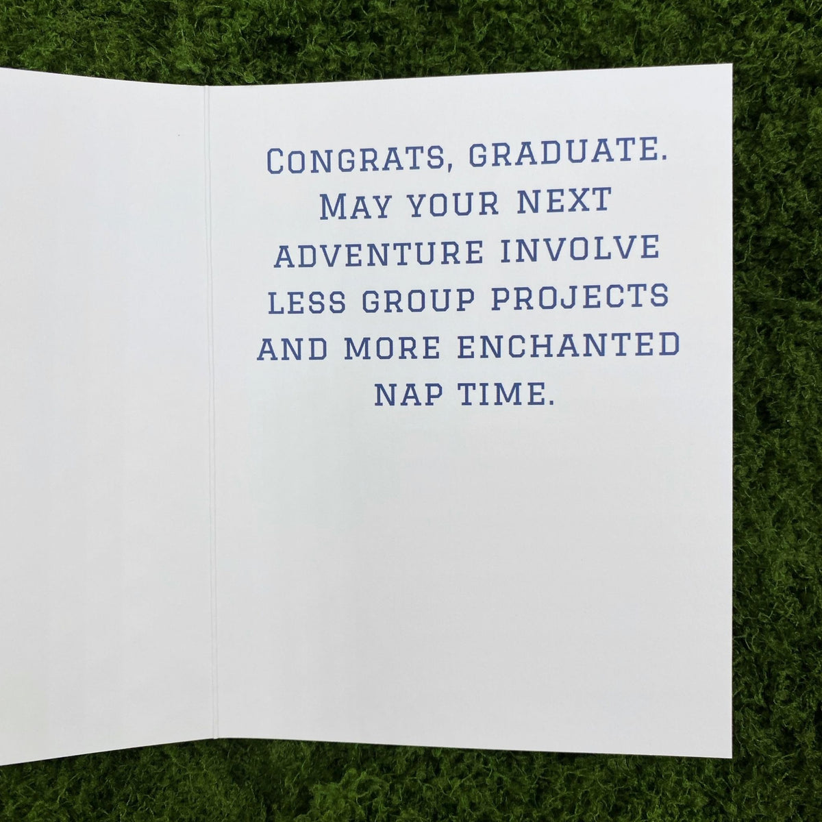 Open interior of the greeting card showing the printed message "Congrats, graduate. May your next adventure involve less group projects and more enchanted nap time."