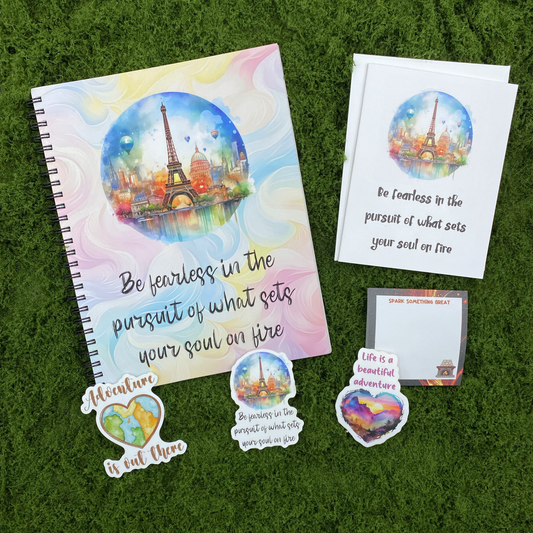 A motivational gift set including a be fearless spiral notebook, a matching greeting card with envelope, a spark something great sticky note pad, and three watercolor die-cut stickers featuring a world map heart, Eiffel Tower scene, and mountain sunset heart, arranged on a green moss surface