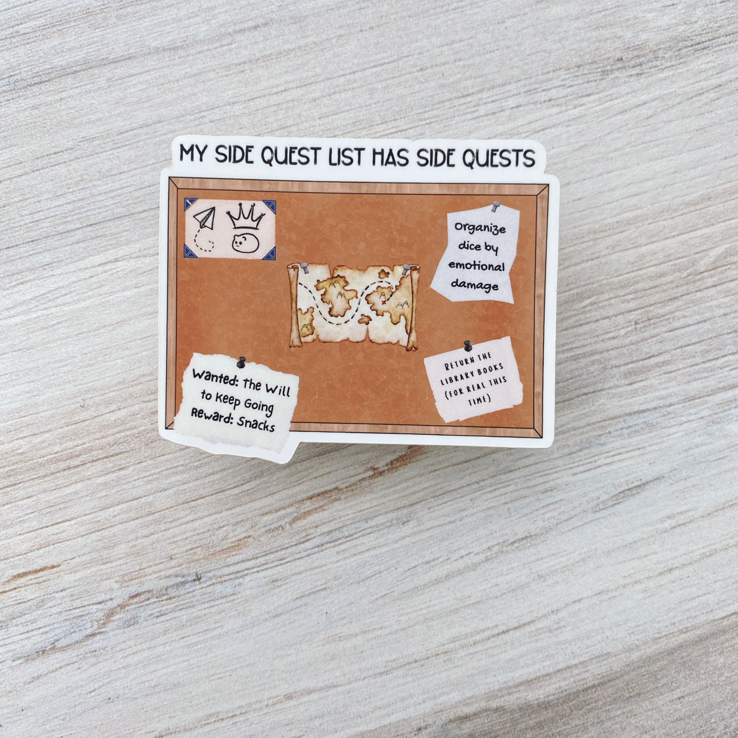 Die-cut vinyl sticker showing a corkboard with a treasure map and notes, with the text "My side quest list has side quests," on a light wood background