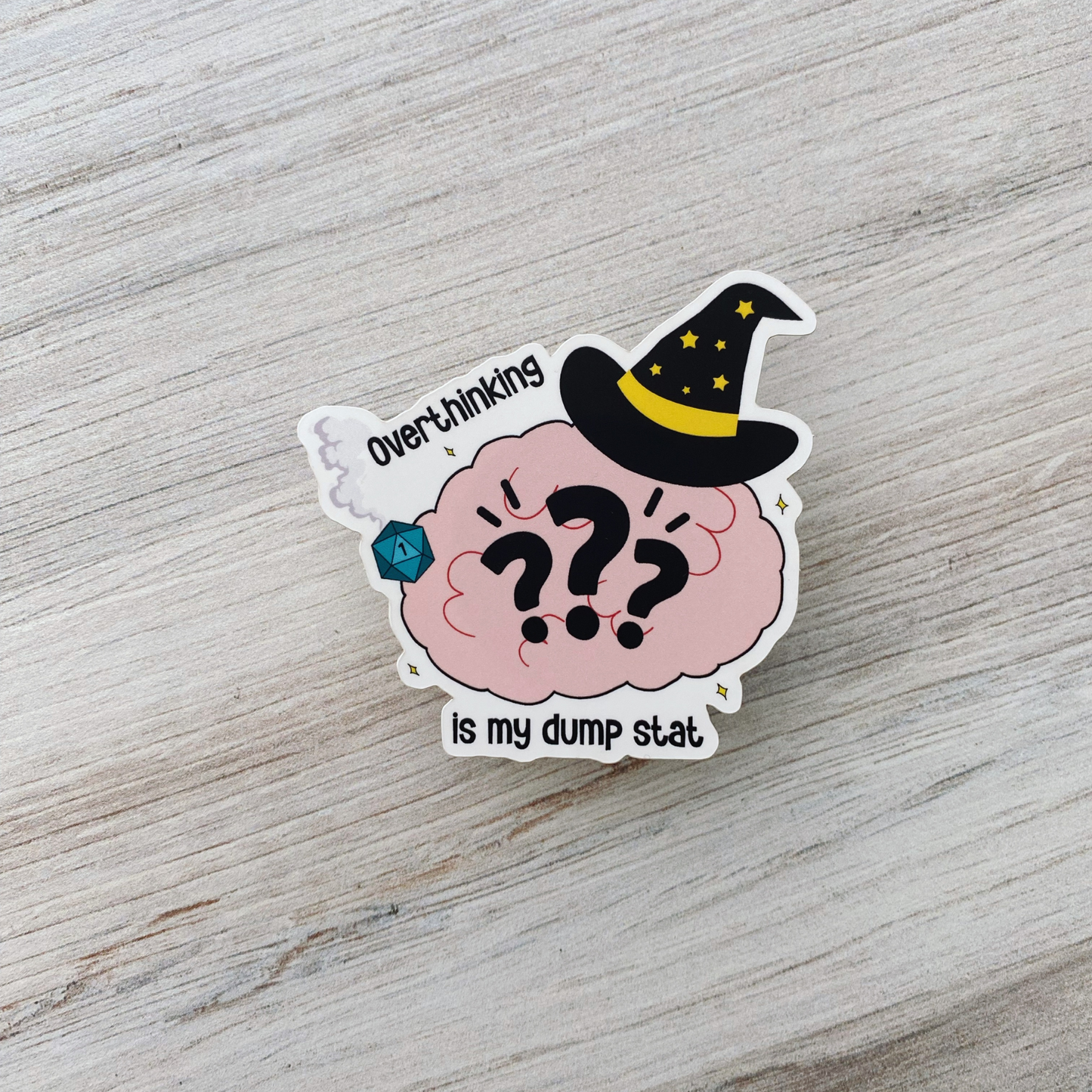 Die-cut vinyl sticker showing a wizard-hatted brain with question marks and a blue d20 showing a 1, with the text "Overthinking is my dump stat," on a light wood background