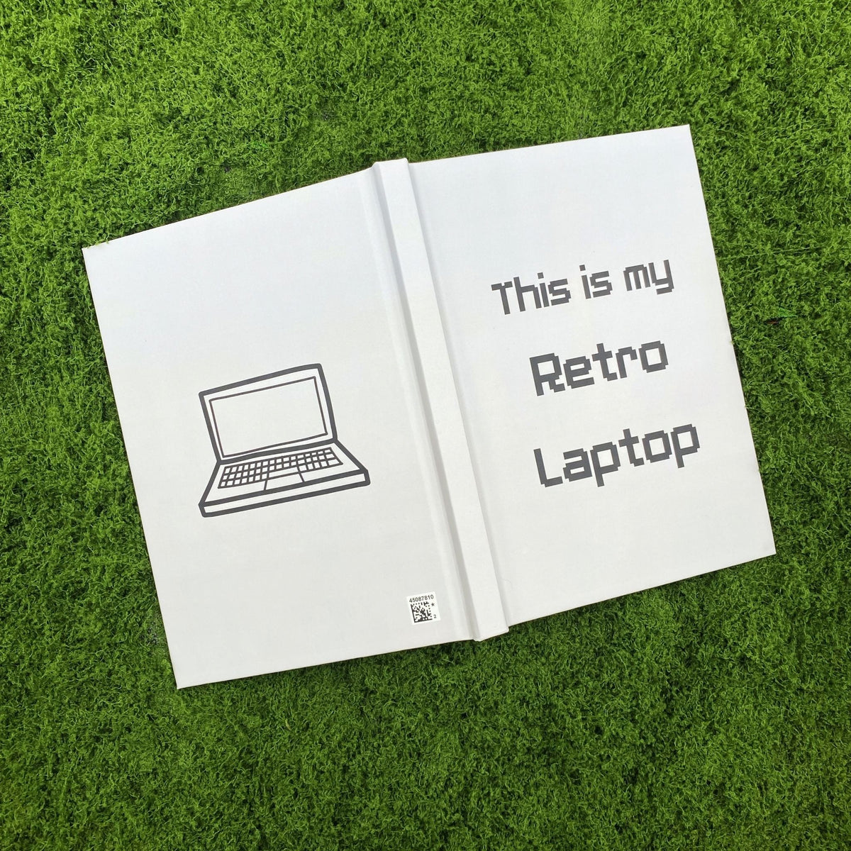 Open light grey hardcover journal showing a simple outlined laptop illustration on the back cover and the 'This is my Retro Laptop' text on the front cover.