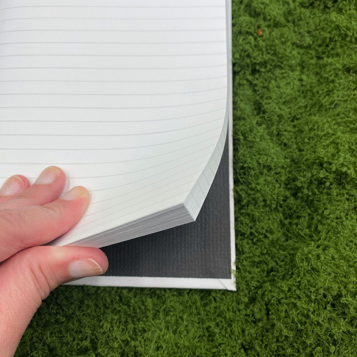 Close-up of a hand fanning through the lined pages of the journal, showing the black interior lining of the hardcover binding.