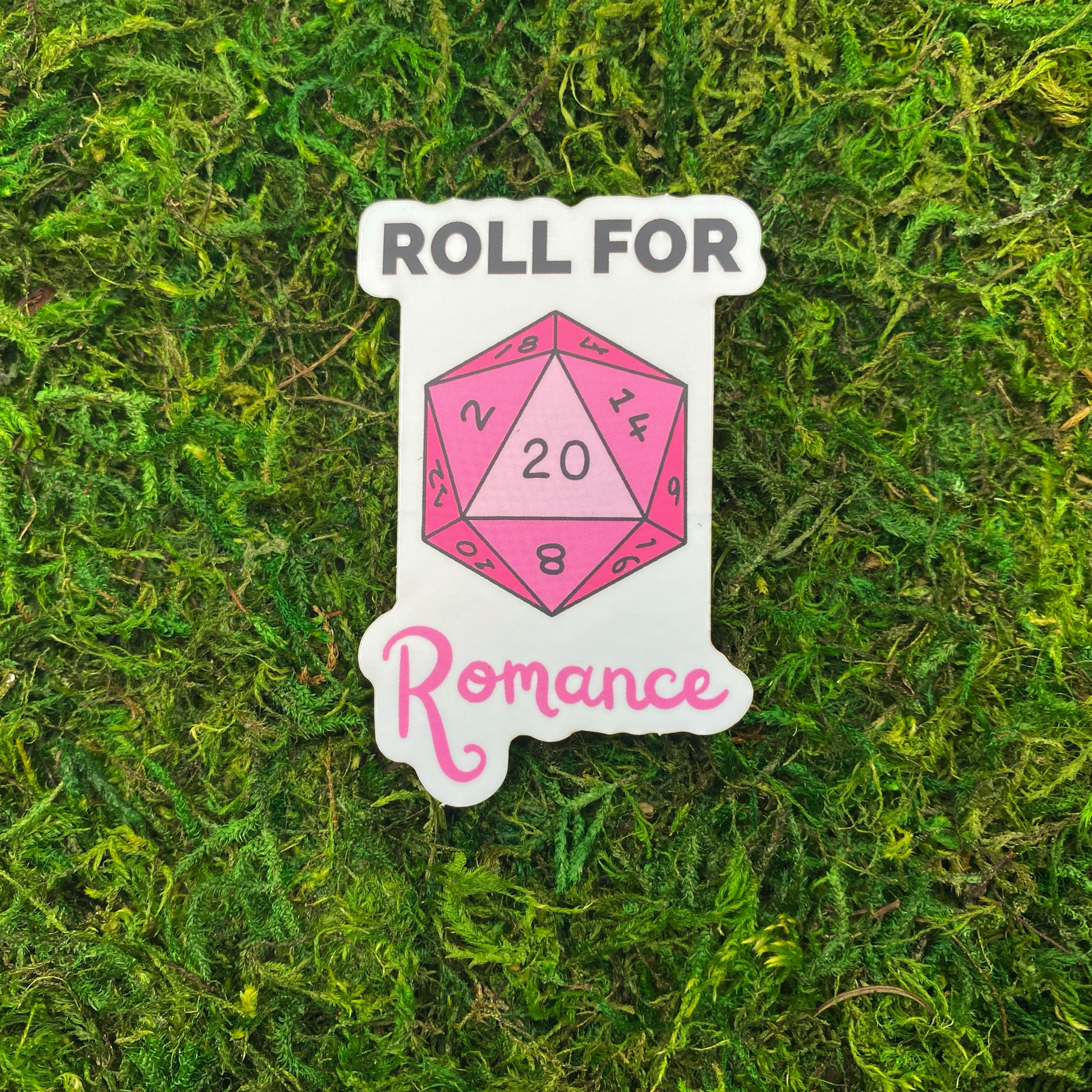 A sticker reading "Roll for Romance" with an illustration of a pink twenty-sided die showing the number 20, resting on artificial moss.