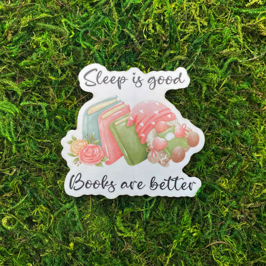 Die-cut sticker with stacked books, a sleeping gnome cradling a book, and the text 'Sleep is good, books are better,' laid on faux moss