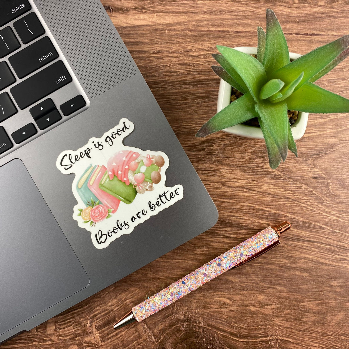 'Sleep is good, books are better' book-themed sticker applied to an open laptop next to a small succulent and glitter pen