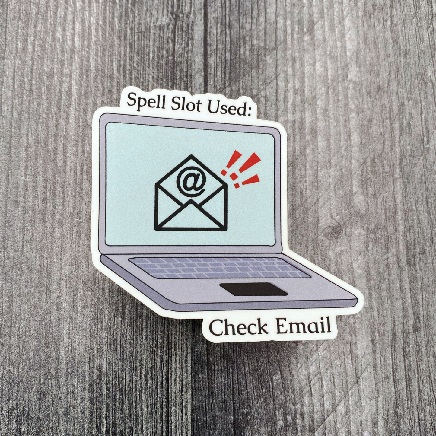 Die-cut vinyl sticker showing a laptop with an email notification, with the text "Spell slot used: check email," on a gray wood background