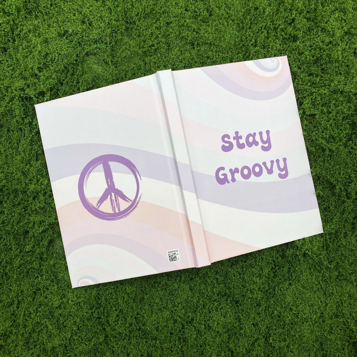 Open hardcover journal showing a hand-drawn purple peace sign on the back cover and the 'Stay Groovy' design on the front cover.
