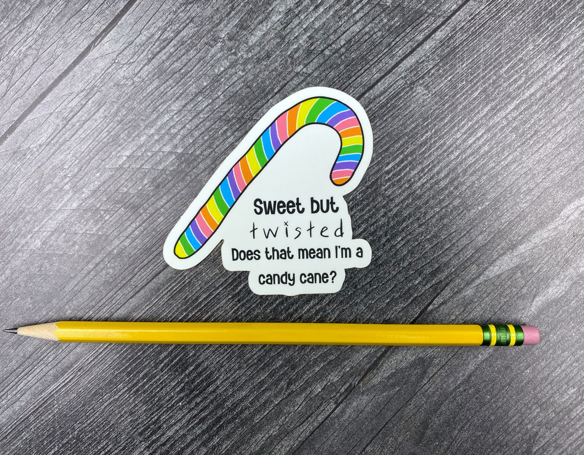 Die-cut vinyl sticker showing a rainbow-striped candy cane with the text "Sweet but twisted, does that mean I'm a candy cane?" on a gray wood background next to a yellow pencil