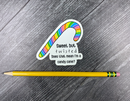 Die-cut vinyl sticker showing a rainbow-striped candy cane with the text "Sweet but twisted, does that mean I'm a candy cane?" on a gray wood background next to a yellow pencil