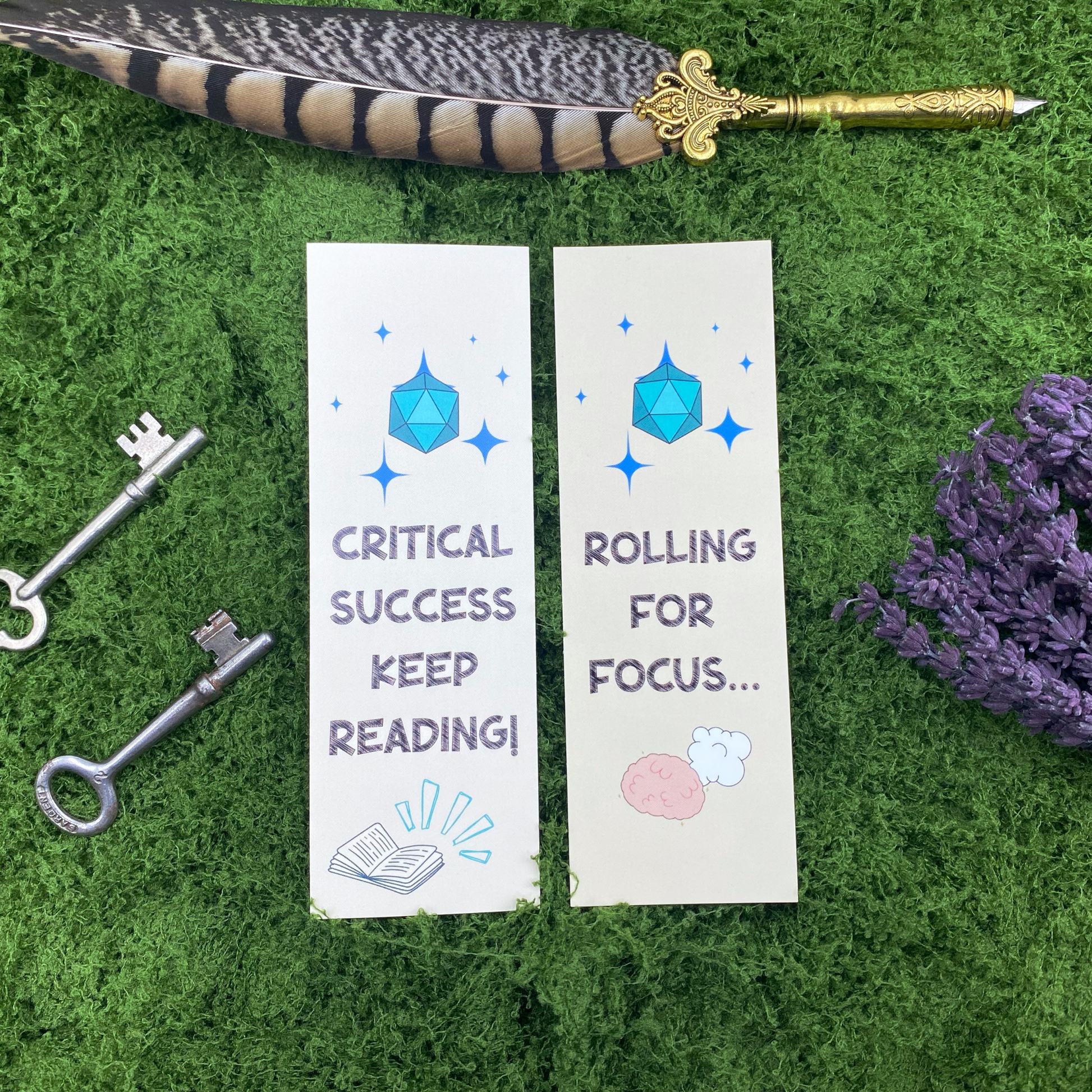 Two sides of a bookmark shown side by side, both featuring a blue d20 die with sparkles, one reading "Critical Success, Keep Reading!" over an open glowing book, the other reading "Rolling for Focus..." over a brain and cloud illustration, resting on artificial grass next to two vintage keys, dried lavender, and a gold quill pen.