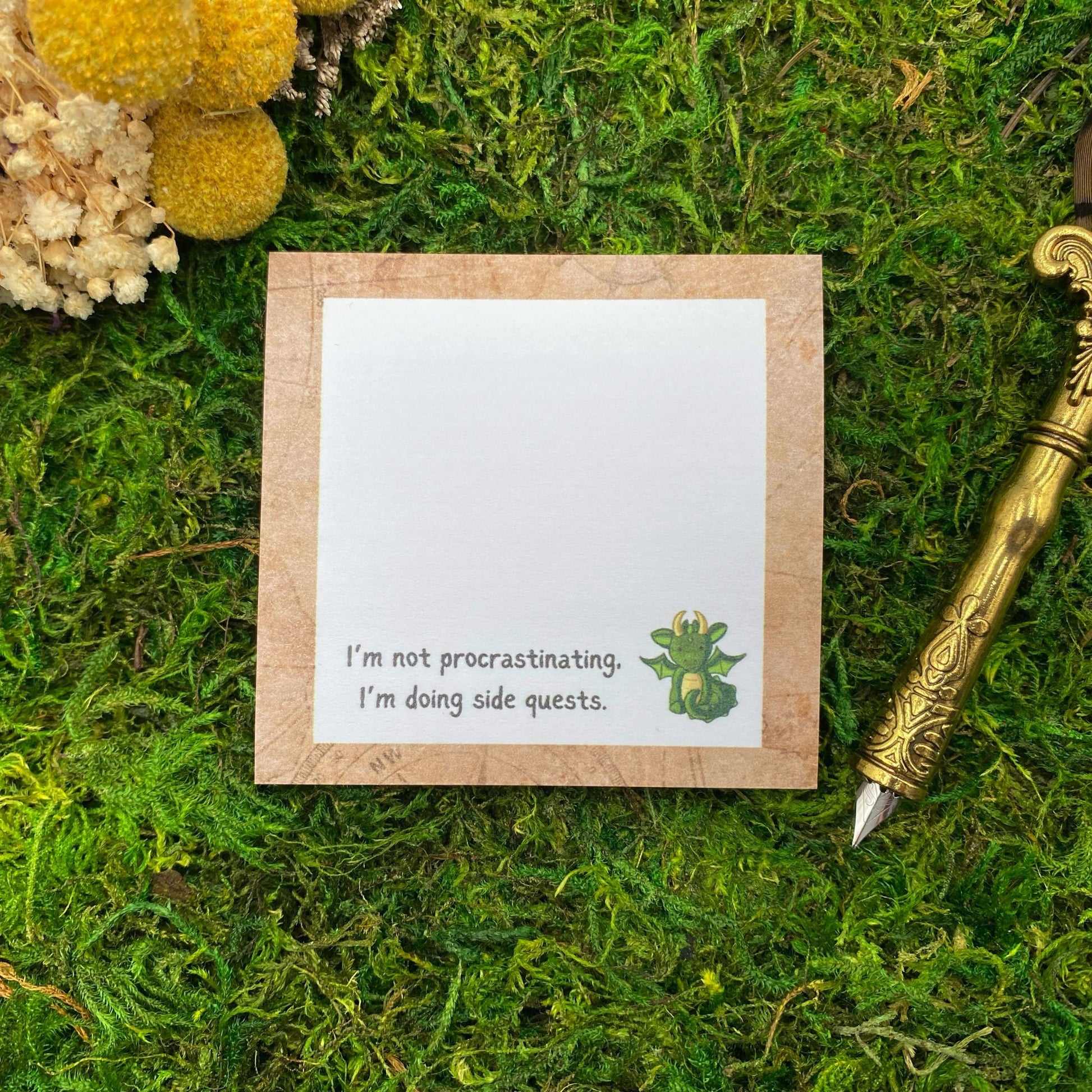 Square sticky note pad with a cartoon green dragon and the text 'I'm not procrastinating, I'm doing side quests,' on a moss background