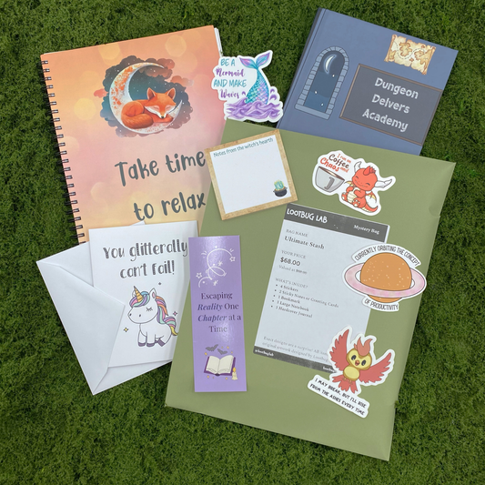 A Lootbug Lab ultimate stash mystery bag with a reveal card surrounded by sample items including stickers, a bookmark, a large notebook, a hardcover journal, and sticky note pads on a green moss surface