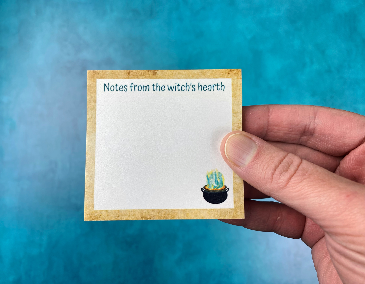 a hand holding a sticky note that says "Notes from the witch's hearth" featuring a cute bubbling cauldron illustration in the lower corner.